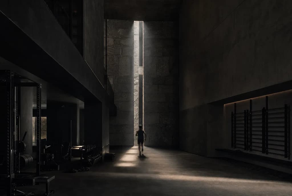 A distant athlete moving through a tall shaft of light in a dark architectural training space.