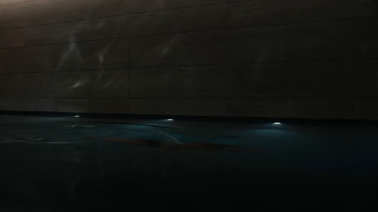 A dark indoor lap pool with slow water reflections moving across honed stone walls.