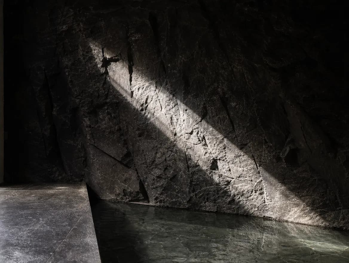 A blade of daylight across rough volcanic basalt above still water.