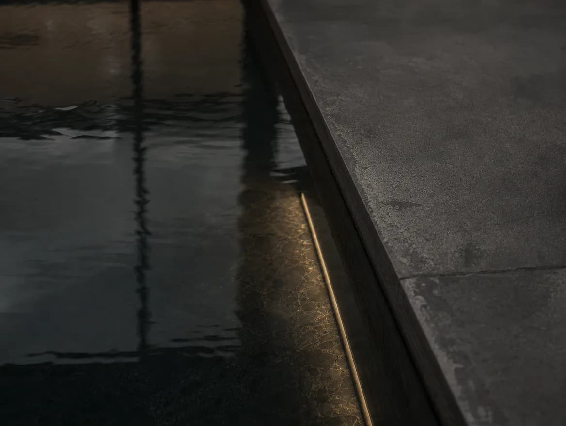 Still black water meeting honed charcoal stone at the pool edge.
